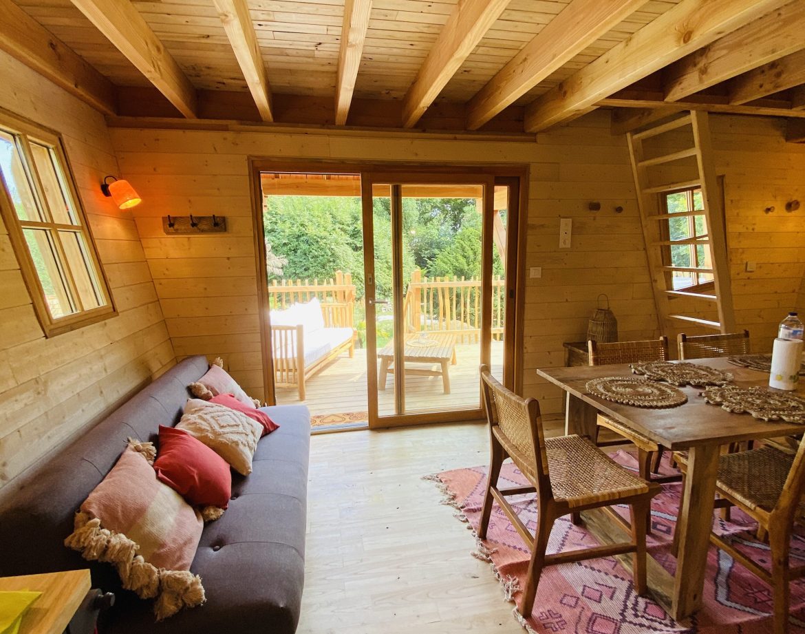 Cabane en bois en Bretagne, intérieur chaleureux avec canapé et vue sur la terrasse.