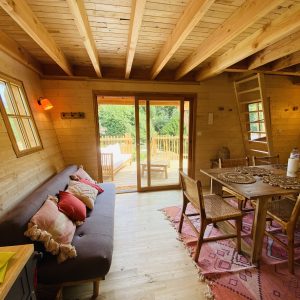 Cabane en bois en Bretagne, intérieur chaleureux avec canapé et vue sur la terrasse.