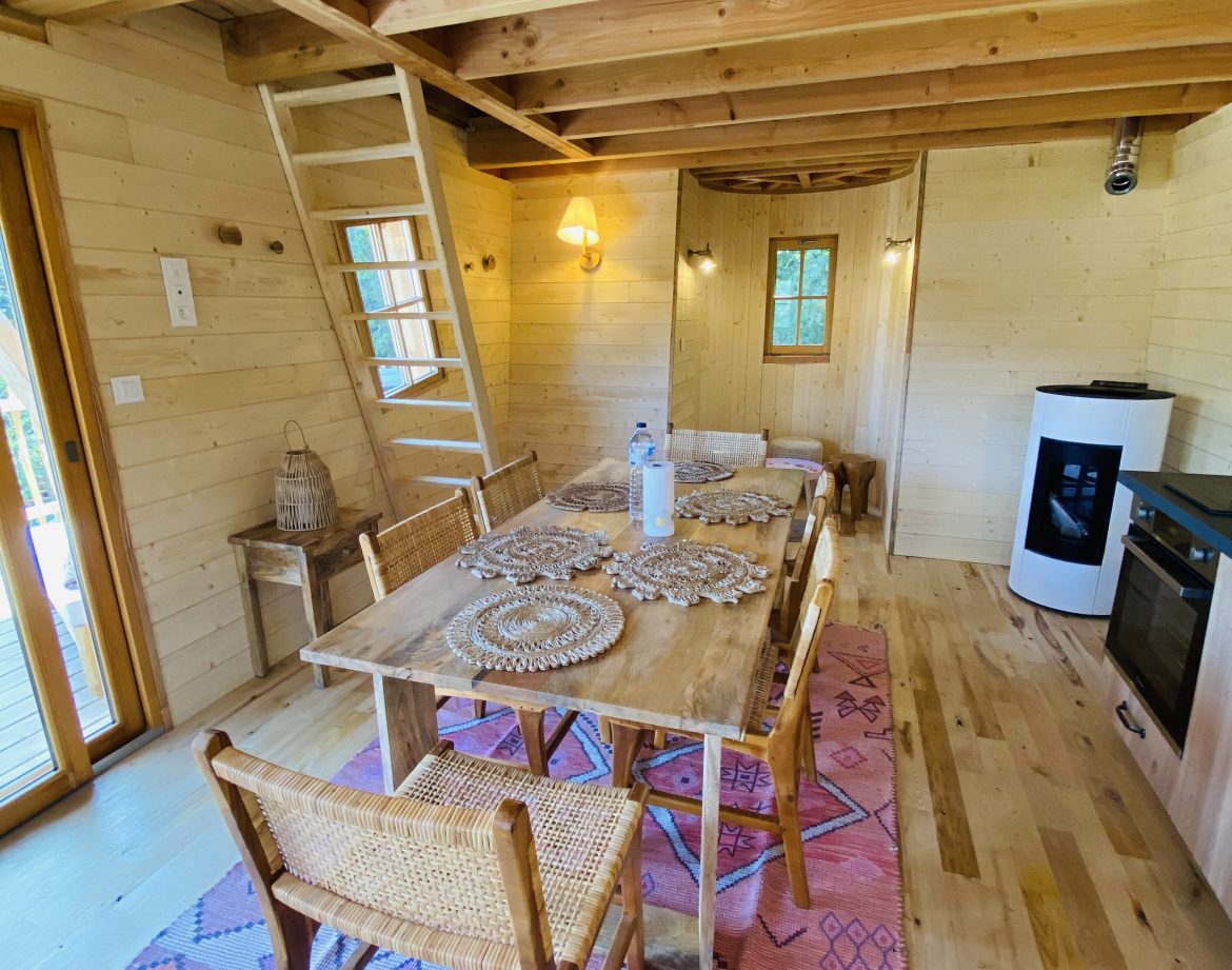 Cabane en bois en Bretagne, intérieur lumineux avec table en bois et tapis coloré.