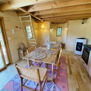 Cabane en bois en Bretagne, intérieur lumineux avec table en bois et tapis coloré.