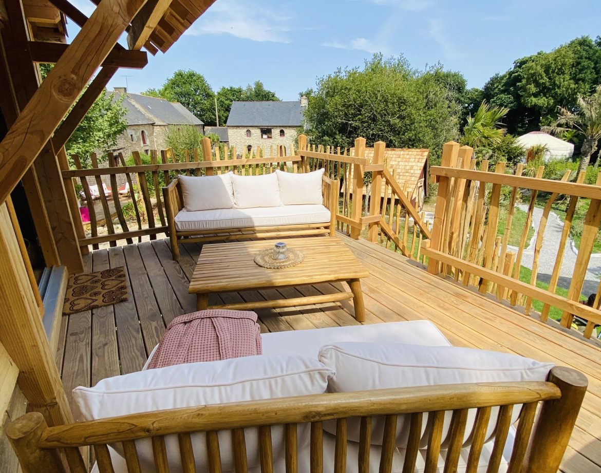 Cabane en bois en Bretagne avec terrasse ensoleillée et mobilier confortable.