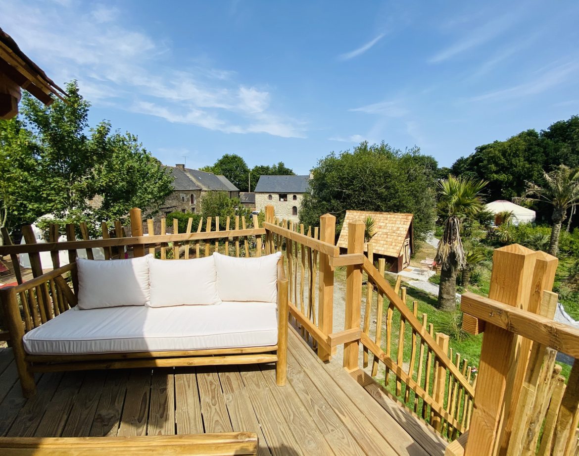 Cabane perchée en Bretagne avec terrasse en bois et vue sur la verdure environnante.