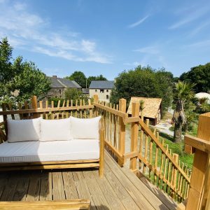 Cabane perchée en Bretagne avec terrasse en bois et vue sur la verdure environnante.