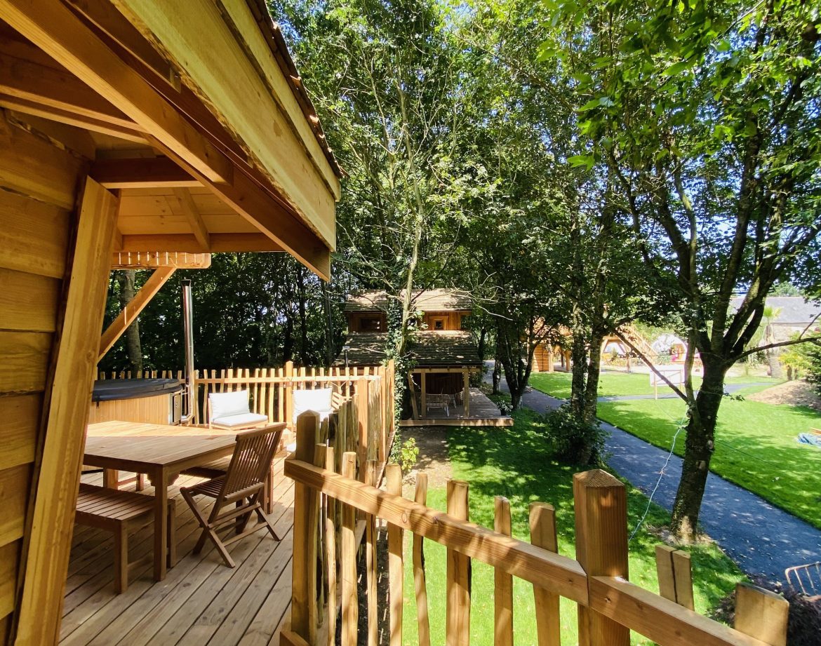 Cabane en bois perchée, entourée darbres, avec terrasse ensoleillée.