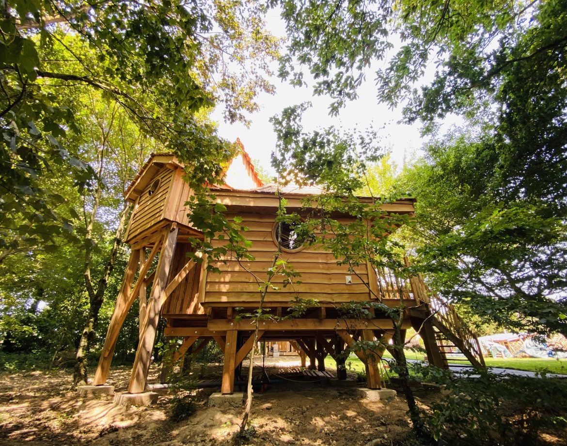 Cabane perchée en bois en Bretagne, entourée darbres verdoyants.