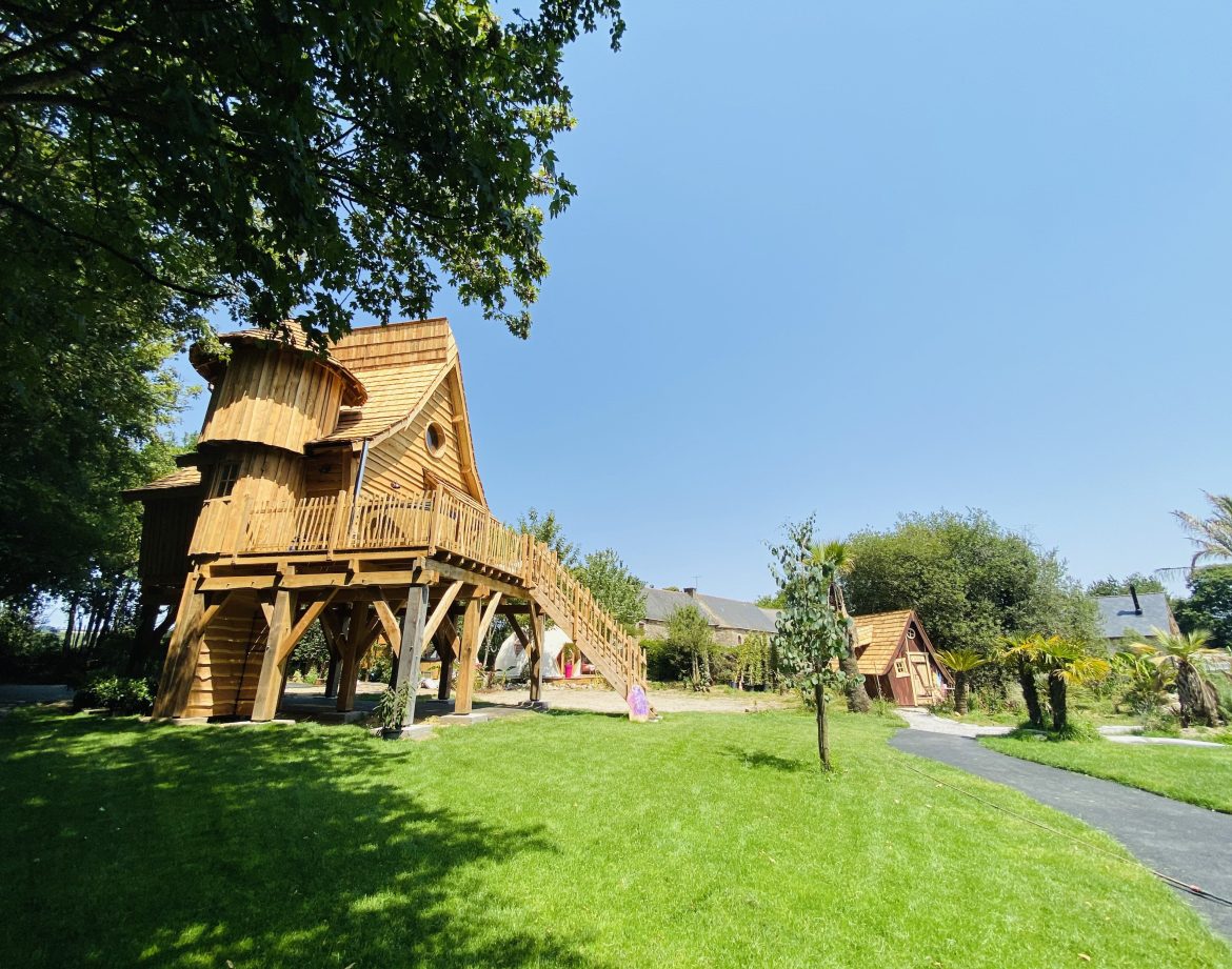 Cabane en bois perchée, entourée de verdure et dun ciel bleu éclatant.