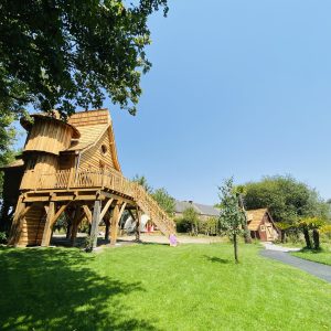 Cabane en bois perchée, entourée de verdure et dun ciel bleu éclatant.