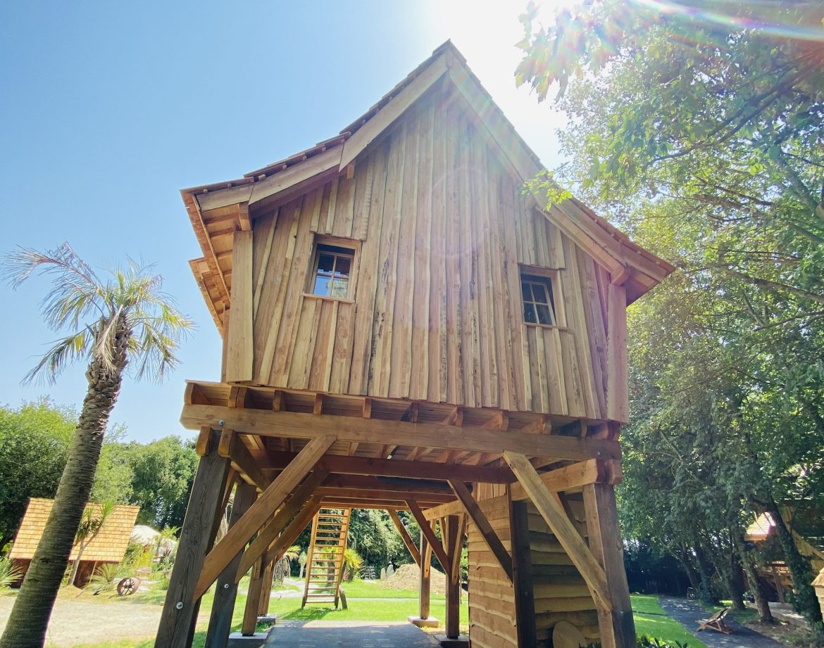 Cabane sur pilotis en bois, baignée de lumière sous un ciel bleu en Bretagne.