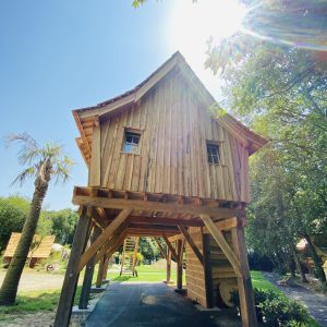 Cabane sur pilotis en bois, baignée de lumière sous un ciel bleu en Bretagne.