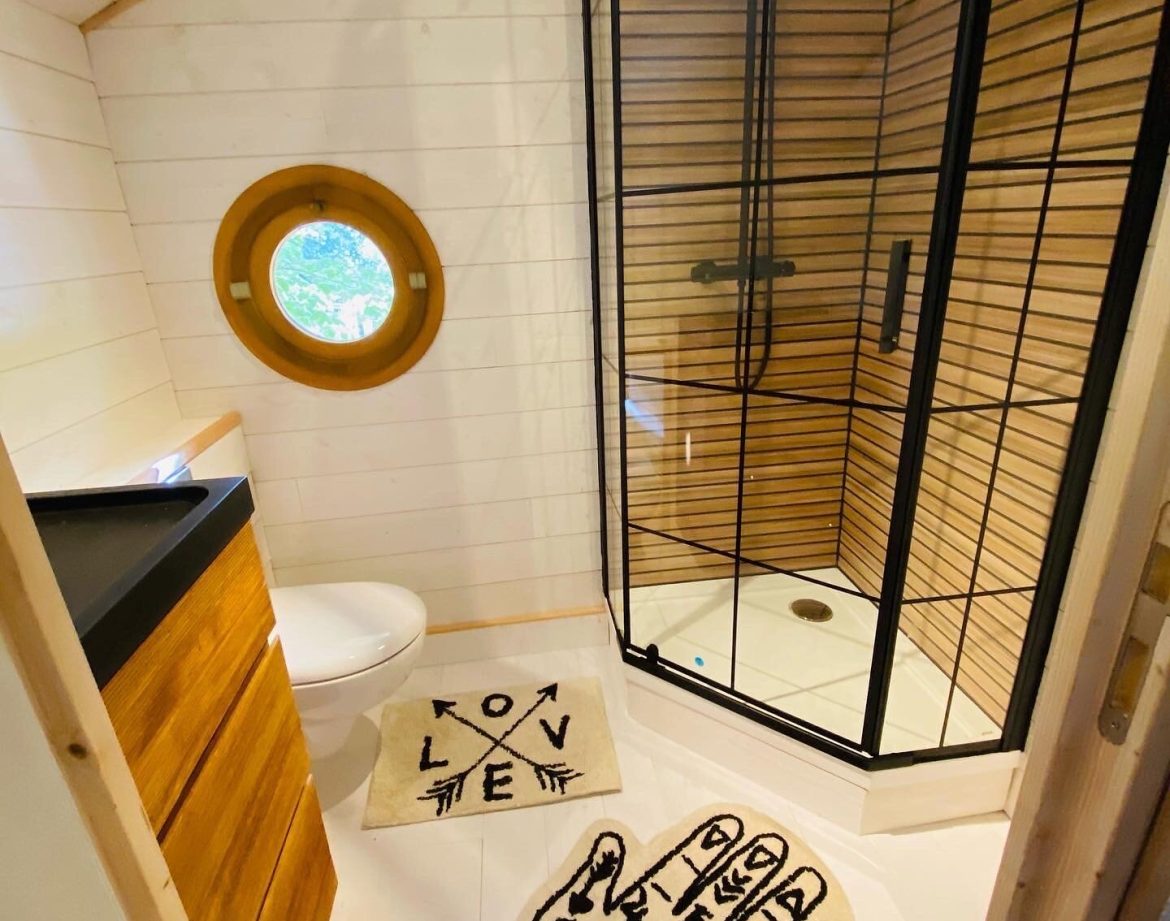Cabane en Bretagne avec douche moderne et fenêtre ronde. Ambiance chaleureuse et originale.