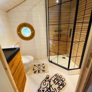 Cabane en Bretagne avec douche moderne et fenêtre ronde. Ambiance chaleureuse et originale.