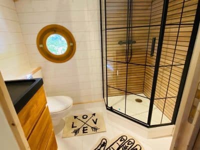 Cabane en Bretagne avec douche moderne et fenêtre ronde. Ambiance chaleureuse et originale.