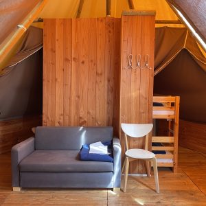 Tente lodge cosy en Midi-Pyrénées, avec canapé et lit superposé en bois.