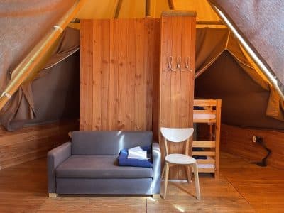 Tente lodge cosy en Midi-Pyrénées, avec canapé et lit superposé en bois.
