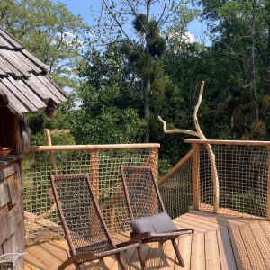 Cabane perchée avec terrasse en bois, chaises longues et vue sur la nature environnante.