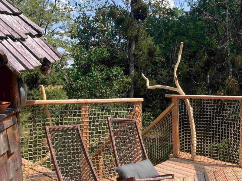Cabane perchée avec terrasse en bois et chaises longues, entourée de verdure.