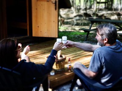 Cabane en bois en Auvergne-Rhône-Alpes, couple trinquant sur une terrasse ensoleillée.