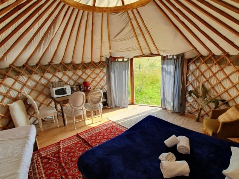 Yourte spacieuse en Midi-Pyrénées, avec un intérieur en bois et un tapis coloré.