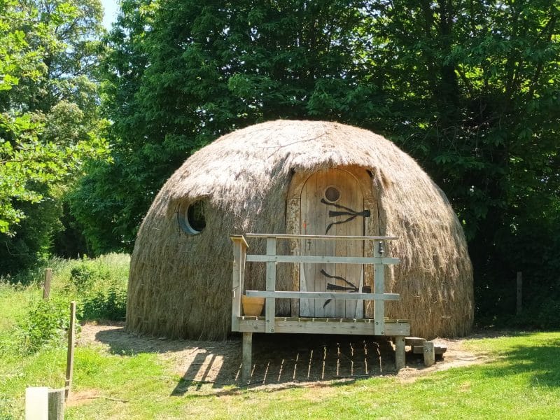 Hébergement insolite en forme de dôme, recouvert de paille, dans un cadre verdoyant.