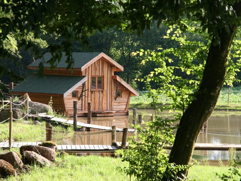 Charmante cabane en bois au bord dun étang, entourée de verdure luxuriante.