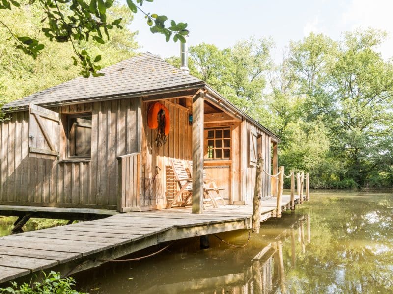 Cabane en bois sur pilotis, entourée dun étang et de verdure luxuriante.