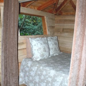 Cabane en bois dans les Pays de la Loire, lit douillet avec rideaux en velours.