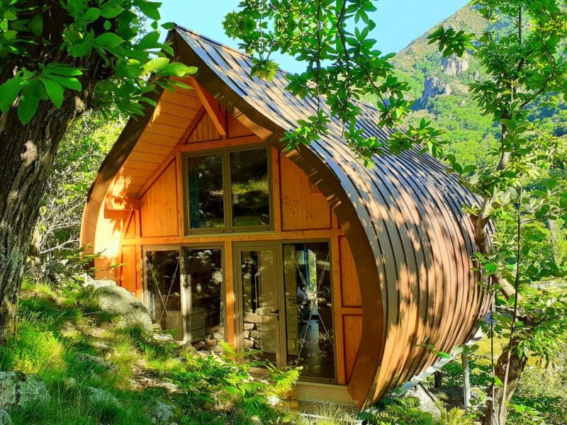 Cabane en bois au milieu de la nature, avec un toit en pente et de grandes fenêtres.