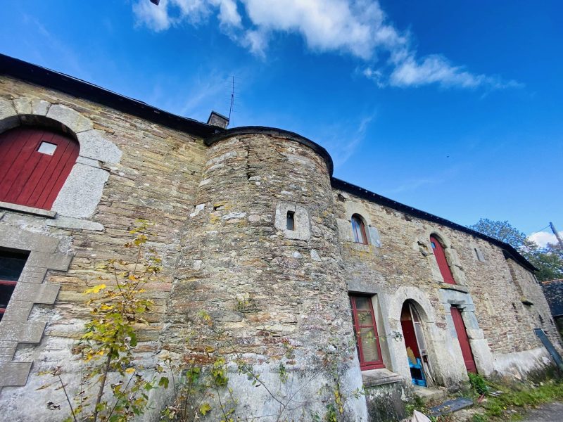 Ancienne grange en pierre avec des volets rouges sous un ciel bleu.