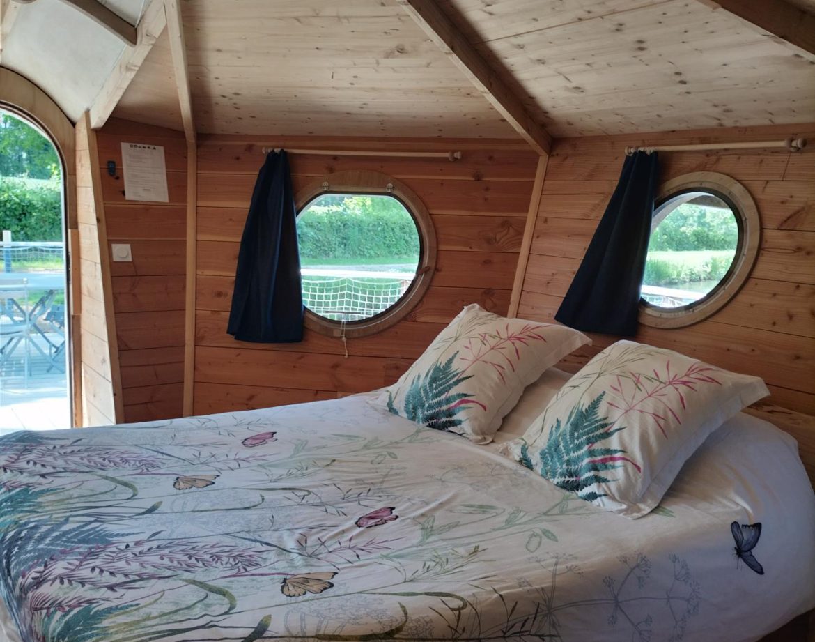 Chalet en bois avec lit douillet et fenêtres rondes, ambiance chaleureuse.