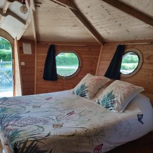 Chalet en bois avec lit douillet et fenêtres rondes, ambiance chaleureuse.