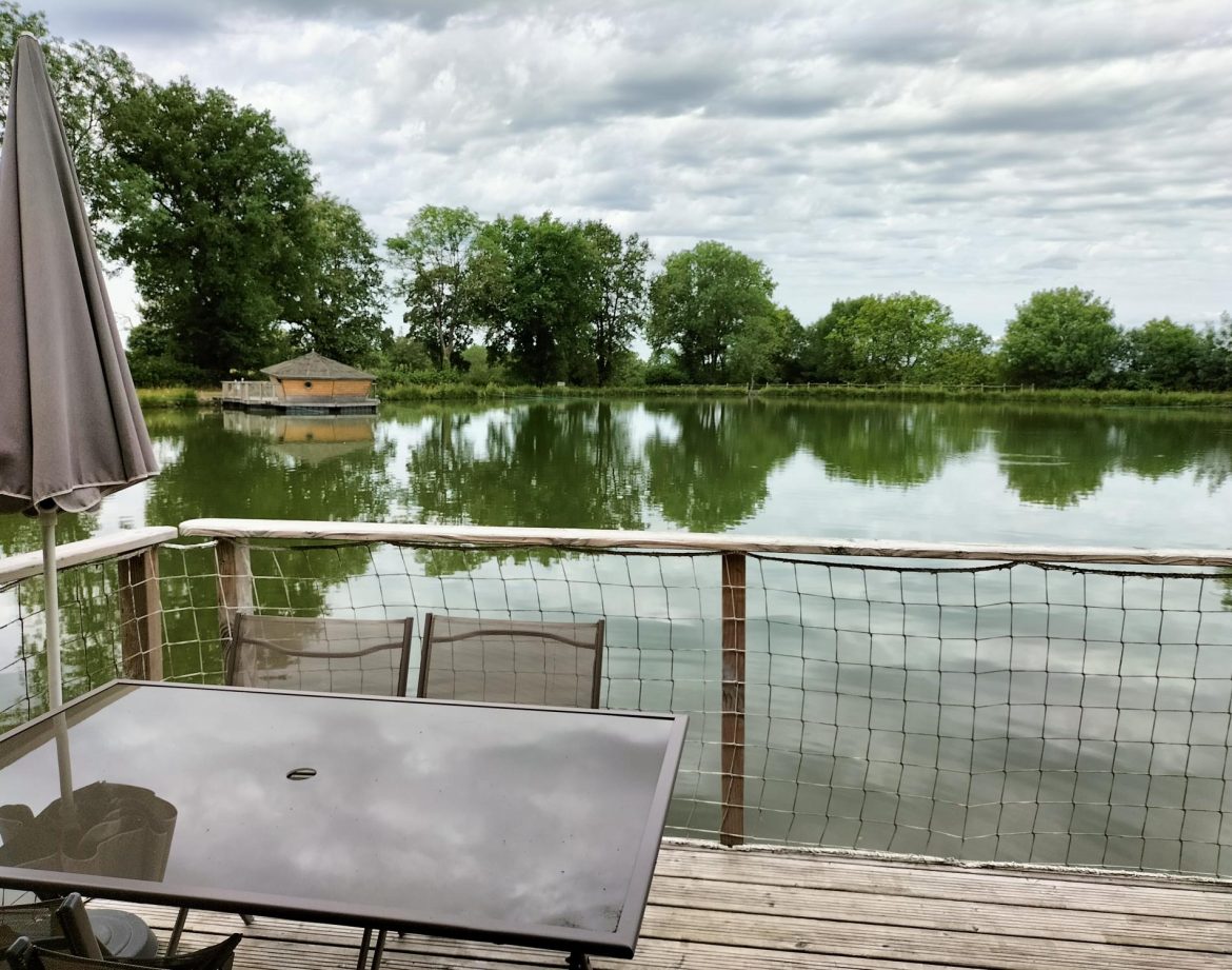Cabane flottante au bord dun lac, avec une terrasse et vue sur la nature verdoyante.