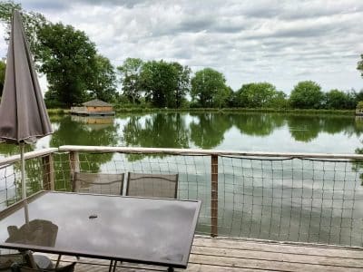 Cabane flottante au bord dun lac, avec une terrasse et vue sur la nature verdoyante.