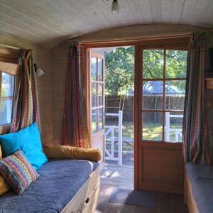 Intérieur dune roulotte cosy avec coussins colorés et vue sur le jardin.