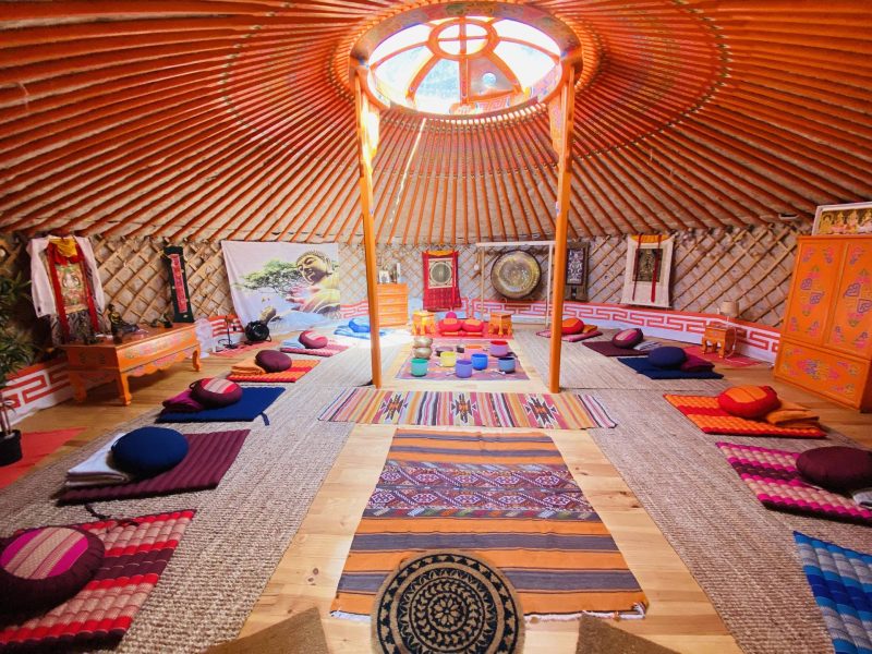Yourte colorée avec des coussins confortables et un éclairage naturel au plafond.