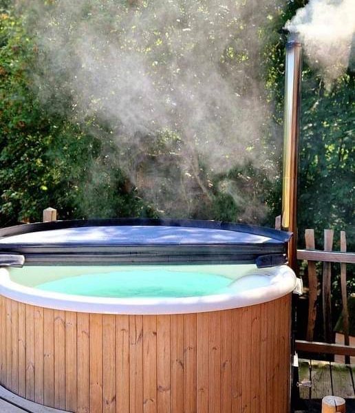 Chalet avec jacuzzi extérieur fumant, entouré de verdure apaisante.