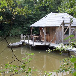 Cabane sur pilotis au bord dun étang, entourée de verdure luxuriante.