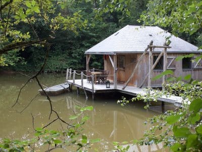 Cabane sur pilotis au bord dun étang, entourée de verdure luxuriante.