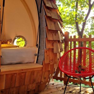 Hébergement insolite en Bretagne : cabane en bois avec un fauteuil rouge sur la terrasse.