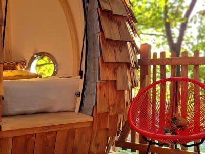 Hébergement insolite en Bretagne : cabane en bois avec un fauteuil rouge sur la terrasse.