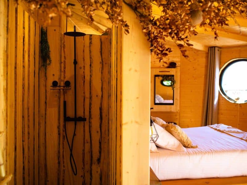 Cabane en bois avec douche moderne et lit douillet, ambiance chaleureuse.