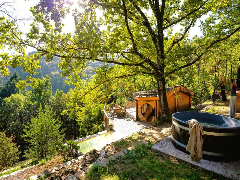 Cabane en bois avec jacuzzi, entourée de verdure et de paysages naturels.