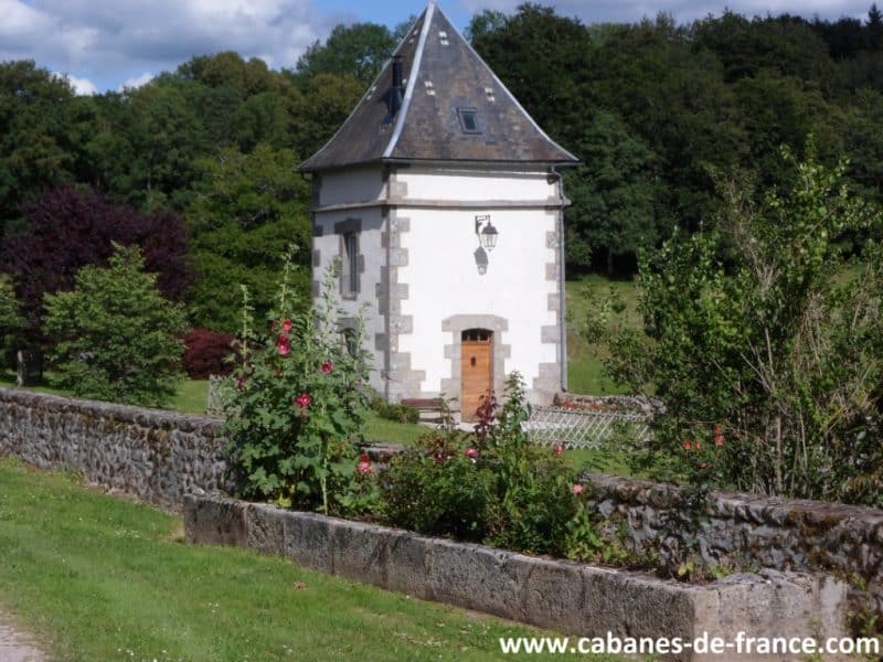 Charmante cabane en pierre avec un toit en ardoise, entourée de verdure.