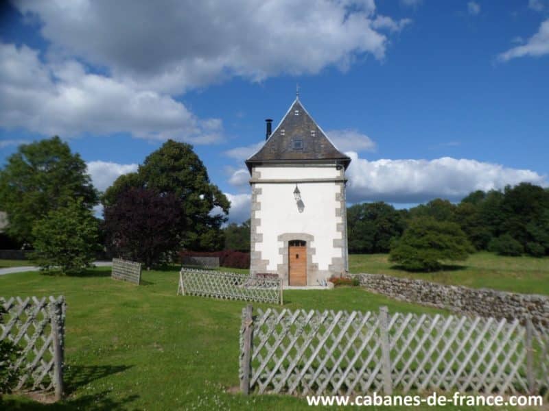 Charmante cabane en pierre avec un toit en ardoise, entourée dun jardin verdoyant.