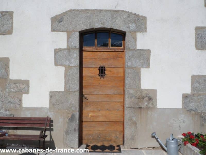 Porte en bois dune cabane rustique, entourée de pierres et de fleurs.