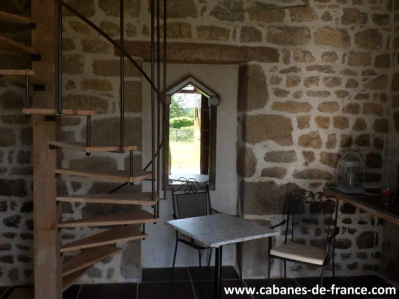 Intérieur dune cabane en pierre avec un escalier en colimaçon et une vue sur le jardin.