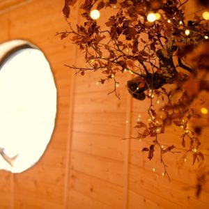 Hébergement insolite en bois avec une fenêtre ronde et des lumières féériques.