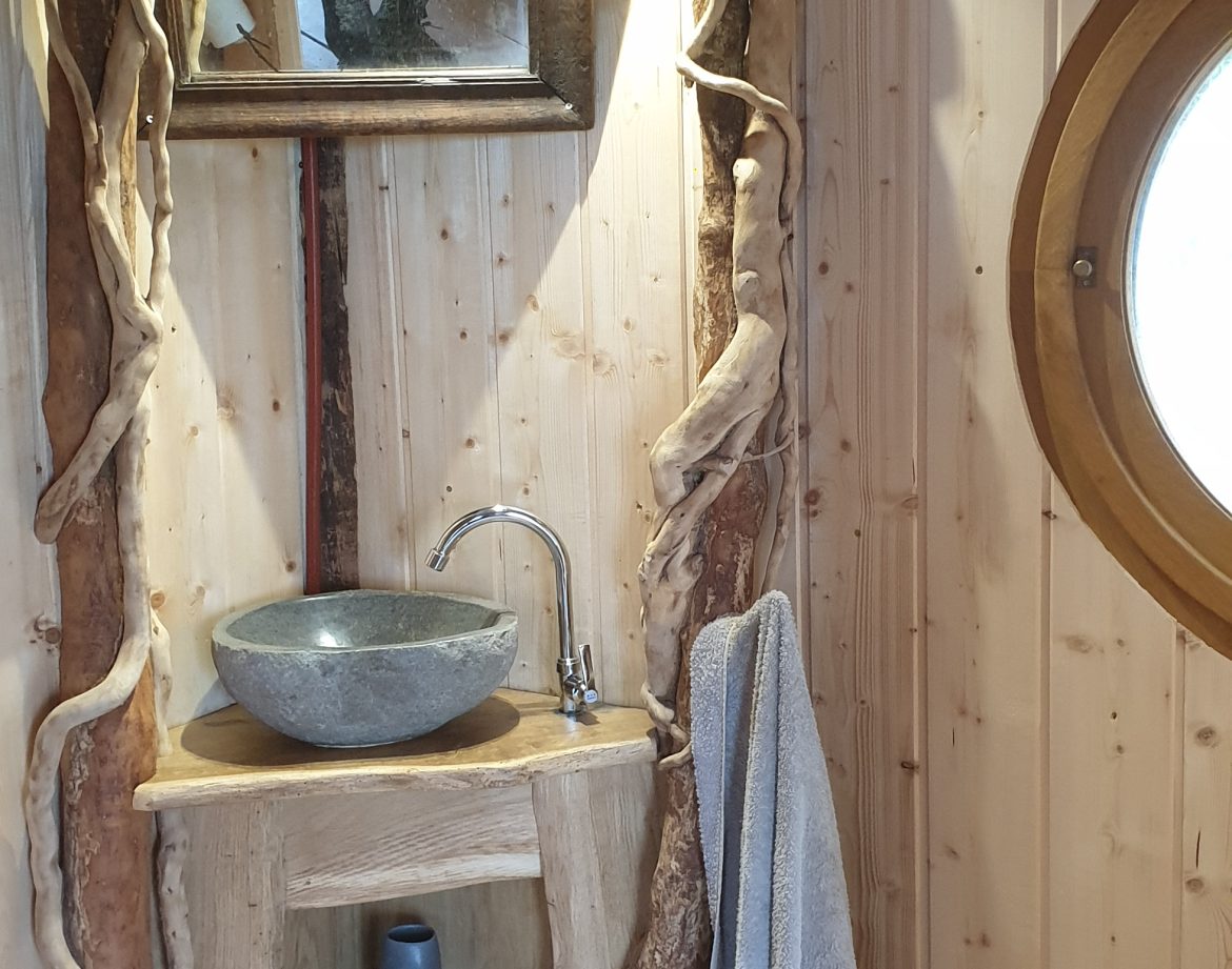 Cabane en bois avec lavabo en pierre et décor naturel, ambiance chaleureuse.