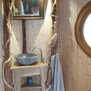 Cabane en bois avec lavabo en pierre et décor naturel, ambiance chaleureuse.