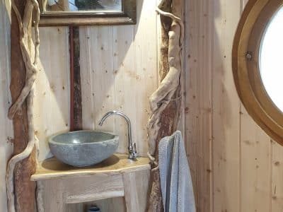 Cabane en bois avec lavabo en pierre et décor naturel, ambiance chaleureuse.