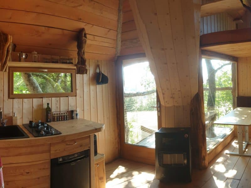 Cabane en bois avec cuisine, grandes fenêtres offrant une vue sur la nature.